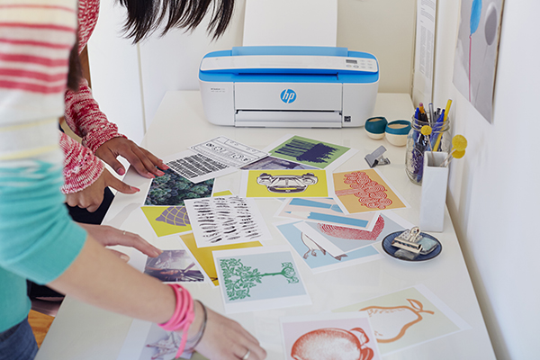 Two girls look through photographs and artwork printed on a HP DeskJet 3720 All-in-One.
